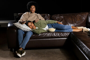 Watching Diverse couple sitting on brown sectional couch in living room, with popcorn and TV remote