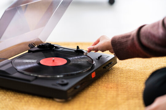 A person's hand is shown placing the needle on a vinyl record spinning on a turntable. They are preparing to listen to music, enjoying the classic sound of analog audio.