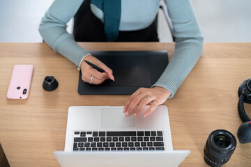 A person is using a drawing tablet and stylus alongside a laptop. They are likely engaged in creative work such as digital art, graphic design, or photo editing, utilizing tools for efficiency.