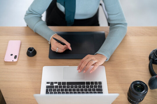 A person is using a drawing tablet and stylus alongside a laptop. They are likely engaged in creative work such as digital art, graphic design, or photo editing, utilizing tools for efficiency.