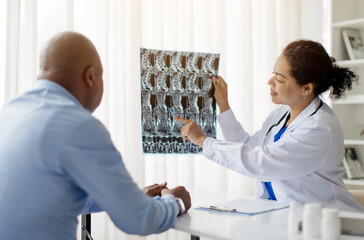 Black Doctor Woman Demonstrating Spinal X-Ray To Male Patient During Meeting In Clinic, Female...