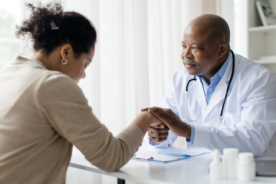 Black Doctor Man Comforting Female Patient After Sharing Bad News At Meeting In Clinic, Friendly Male Physician Soothing Stressed Woman, Holding Her Hand After Telling Bad Diagnosis, Selective Focus