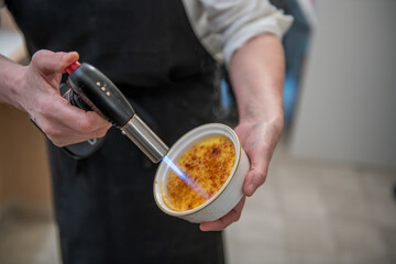 Chef preparing creme brulee with torch flame in elegant kitchen setting