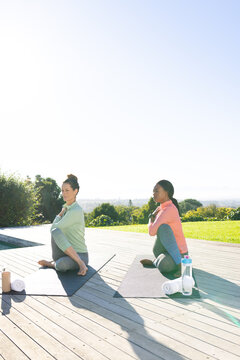 Twisting spines Diverse female friends on wooden deck overlooking city, with yoga mats and towels