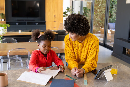 Studying Diverse mother and daughter at kitchen island with notebook, pencils and tablet, sunshine