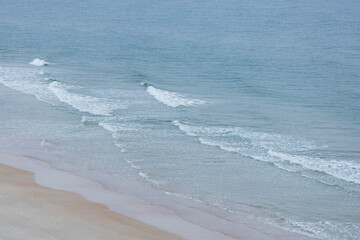 Tranquil coastal scene at sunrise with soft ocean waves rolling onto the shore and birds flying peacefully through the pastel morning sky. The gentle light of dawn creates a dreamy and serene atmosphe