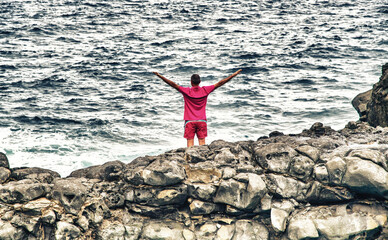 Man relaxing and embracing nature standing on the rocks above the ocean. Holiday concept.