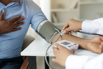 Closeup of doctor measuring arterial blood pressure for male patient, female nurse using stethoscope to measure tension of african american man touching his chest in discomfort, cropped
