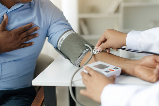 Closeup of doctor measuring arterial blood pressure for male patient, female nurse using stethoscope to measure tension of african american man touching his chest in discomfort, cropped