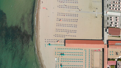 Drone shot of a vibrant beach club with rows of umbrellas and clear blue sea in the background