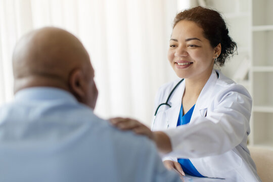 Portrait of black female doctor tapping male patients shoulder for empathy and encouragement during appointment in modern clinic. General practitioner cheering man at office