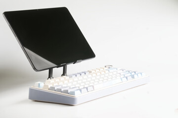 A slim modern digital tablet on a minimalist stand paired with a pastel mechanical wireless keyboard, ideal for ergonomic desk setups and creative digital workflows. Photo