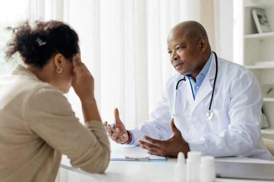 African American doctor speaking seriously with woman patient during meeting in clinic, upset black female holding her head in distress during medical consultation, listening diagnosis