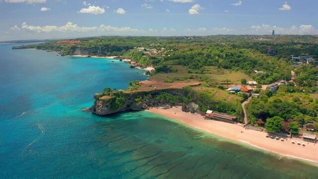 Aerial, lens flare flying above luxury bungalow tourist resort and new kuta golf course at the rim of the rocky and cliffy coastline overlooking vast blue ocean