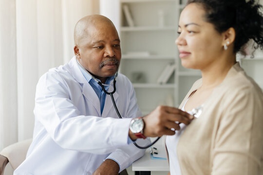 Mature doctor checking lungs of black female patient during medical checkup in clinic, friendly therapist man using stethoscope to examine breathing and heartbeat of young patient, closeup shot