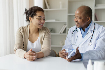 Black Doctor Man Showing Clipboard With Test Results To Curious Female Patient, Professional Male...
