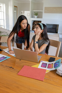 Collaborating Asian friends reviewing app mockups inside living room, with laptop and smartphone