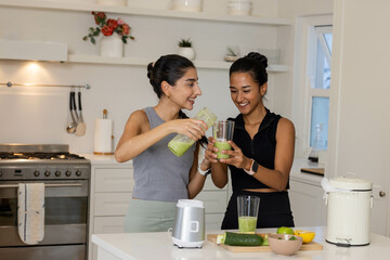 Diverse female friends preparing green smoothies at kitchen island, with blender jug