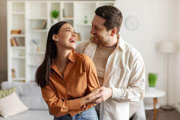 Loving man embracing his wife while dancing in living room, couple enjoying time together. Happy...