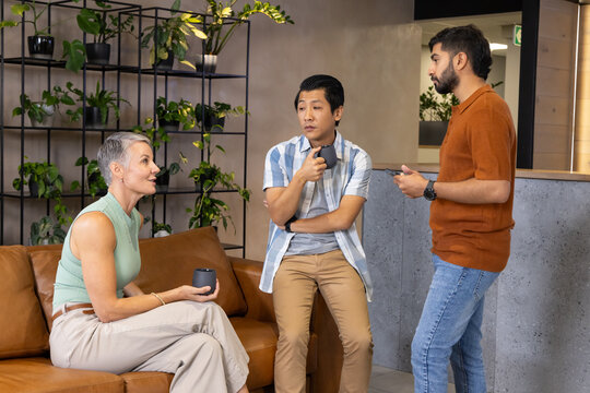 Chatting Diverse coworkers sharing ideas in modern office lounge, with coffee mugs and smartphones