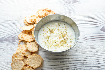diet chips and hummus dip in metal bowl on white wooden background in close-up