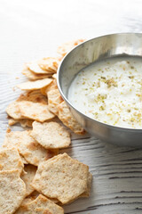 diet chips and hummus dip in metal bowl on white wooden background in close-up
