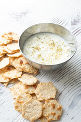 diet chips and hummus dip in metal bowl on white wooden background in close-up