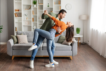 Romantic young husband and wife dancing, having fun at home, enjoying domestic date, living room interior, full length. Happy marriage concept