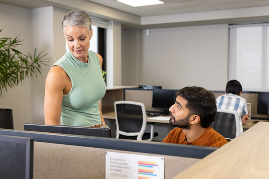 Leaning Diverse coworkers discussing data at open-plan office, with computer monitors