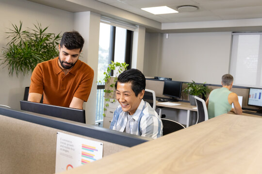 Collaborating diverse male coworkers editing documents at open-plan office, with dual monitors
