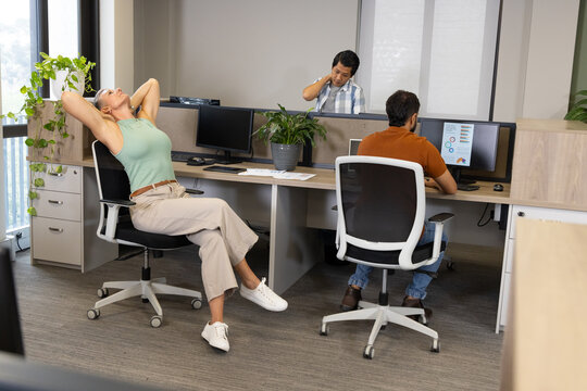 Diverse coworkers working and stretching in open-plan office, with computer monitors, copy space