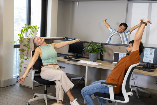 Stretching Diverse coworkers taking break at office desks, with ergonomic chairs and monitors