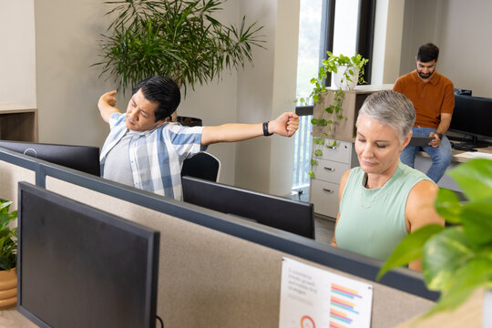 Stretching Diverse coworkers taking short breaks at open-plan office desks, with computer monitors