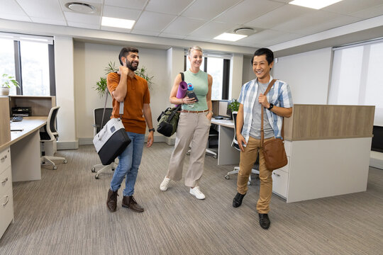 Diverse coworkers walking into modern open-plan office, carrying gym bags and rolled yoga mat - Powered by Adobe