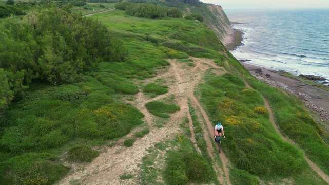 aerial view Latin cyclist woman riding gravel bike on a cliff by the sea at sunrise