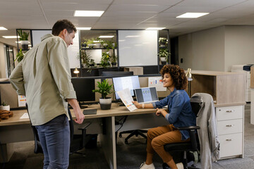 Discussing charts Diverse coworkers collaborating in open plan office, with monitors