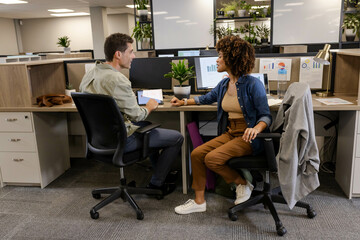 Reviewing charts at open plan office desks, diverse coworkers using tablet and monitors