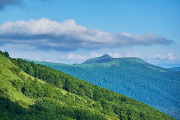 A lush green mountain range stretches under a dynamic sky filled with billowing clouds. Rolling hills, forested slopes, and a distant peak create a tranquil and scenic landscape summer Carpathian.