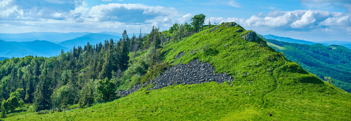 A lush green mountain range stretches under a dynamic sky filled with billowing clouds. Rolling...