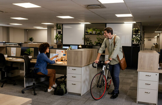 Reviewing printed documents and chatting at open-plan office desk, with bicycle and potted plants