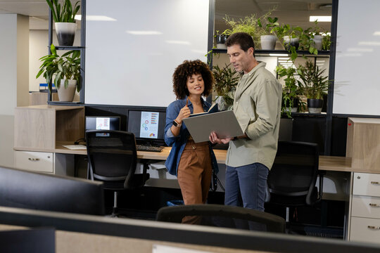 Diverse coworkers collaborating on brainstorming ideas in open office, with laptop and whiteboards