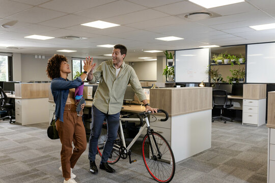 High-fiving Diverse coworkers sharing fitness break in modern office with purple yoga mat, bicycle