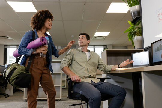 Discussing diverse coworkers sharing plans in open plan office, with purple yoga mat and laptop - Powered by Adobe