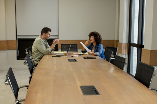 Discussing Diverse coworkers reviewing documents around conference table in boardroom, with laptop