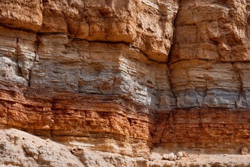 Fototapeta premium Textured rock formations reveal various layers of sediment, showcasing earthy tones of orange, brown, and gray in an outdoor setting illuminated by sunlight