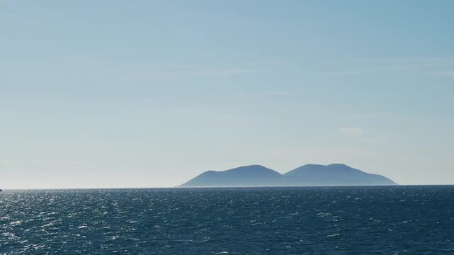 Serene ocean view with distant mistic lonely island on the horizon and clear skies