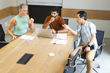 Diverse coworkers working in modern conference room, reviewing printed charts and sticky notes