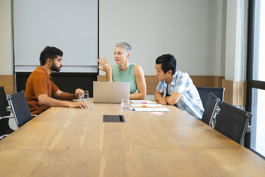 Diverse coworkers discussing project details in meeting room, with silver laptop and sticky notes