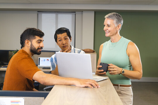 Collaborating Diverse coworkers leaning at counter in open-plan office, with laptop and coffee mug