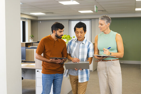 Reviewing Diverse coworkers consulting laptop in modern office workspace, with tablet and notebook